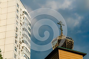 Dome of a small Orthodox church with a cross and a modern high-rise building