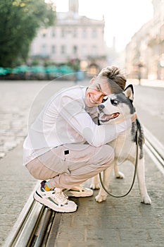 Domestic animals, dogs and people concept. Happy smiling young man hugging his cute husky dog, walking in the city