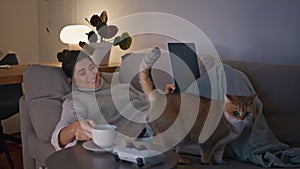 Domestic brunette drinking coffee cup lying sofa with laptop at evening room