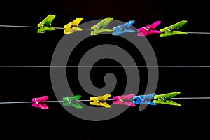 Colorful plastic clothespins in a row on a clothes lines on a black background.