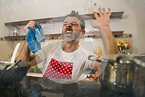 Domestic chores stress - young attractive overworked and depressed man in red apron at home kitchen feeling stressed and tired of