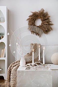 Domestic and cozy christmas living room interior with corduroy sofa, white shelf, candlestick with candle, christmas wearth,