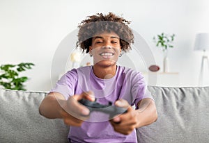 Domestic entertainments. Joyful black teen guy with joystick playing online computer games on couch at home