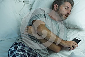 Domestic lifestyle high angle portrait of young attractive and tired man sleeping on bed holding mobile phone in internet and