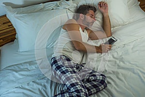 Domestic lifestyle high angle portrait of young attractive and tired man sleeping on bed holding mobile phone in internet and