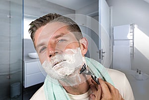 Domestic lifestyle morning portrait of attractive and happy man shaving at modern apartment  bathroom his face covered with foam