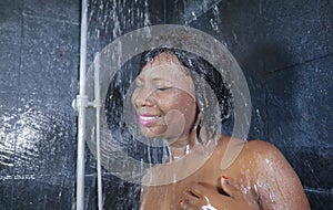 Domestic lifestyle portrait of young happy and beautiful black afro American woman smiling happy taking a shower at home bathroom