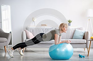 Domestic sports. Athletic mature woman standing in plank on fitness ball, working out core muscles at home