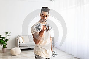 Domestic training concept. Strong young Arab man exercising with dumbbells at home