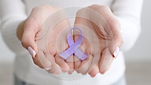 Domestic violence awareness symbol. Close up shot of female hands hands holding purple ribbon, expressing love and unity