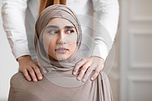 Domestic Violence, Muslim Husband Touching Shoulders Of Scared Wife Indoors photo