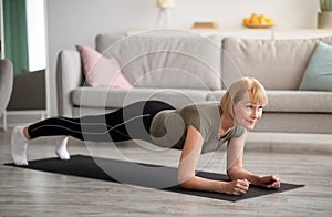 Domestic workout concept. Athletic senior woman standing in elbow plank on yoga mat at home