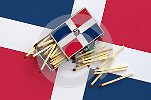 Dominican Republic flag is shown on an open matchbox, from which several matches fall and lies on a large flag