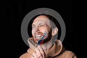 Close-up portrait of young emotive man rips three colors duct tape off his mouth isolated on dark background. Censorship