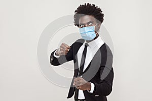 Don`t come any closer! Portrait of angry man in black suit with surgical medical mask standing with boxing fists and ready to