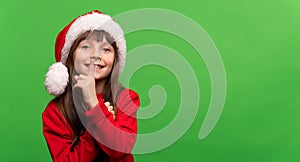 Don't give a surprise. Cute smiling little Santa girl in a hat put her finger to her lips. Silence sign. New Year