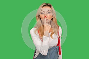 Don`t lie to me! Portrait of angry adult blond woman in denim overalls touching nose with finger