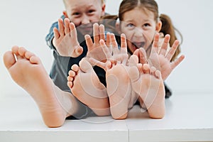 Don't tickle. Little siblings sitting on a table with bare feet. Stop gesture