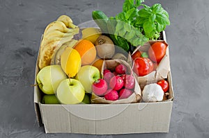 Donation box with fresh organic fruits, vegetables and herbs on a concrete background. Proper nutrition.