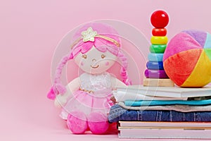 Donation, charity concept. Stuffed soft doll, baby stacking rings pyramid, kid clothes and books over pink background