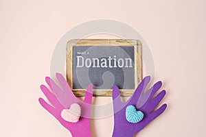 Donation and charity creative background with colorful paper hands holding heart shape and sign board. Top view, flat lay