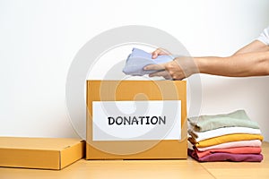 Donation, Charity, Volunteer, Giving and Delivery Concept. Hand holding Clothes into Donation box at home or office for support