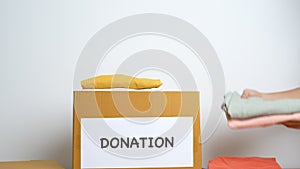 Donation, Charity, Volunteer, Giving and Delivery Concept. Hand holding Clothes into Donation box at home or office for support