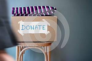 Donation Concept. Donate Box with Used Old Clothes on Chair against Wall in Public Space. blurred walking people as forground