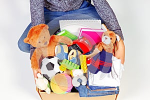 Donation concept. Kid holding donate box with clothes, books, school supplies and toys, white background