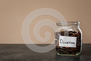 Donation jar with coins on table against color background.