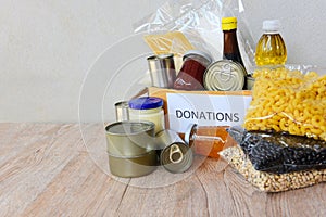 Donations box with canned food on wooden table background / pasta canned goods and dry food non perishable with pea cooking oil