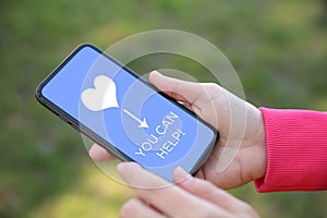 Donations concept. Woman holding smartphone with text YOU CAN HELP, closeup