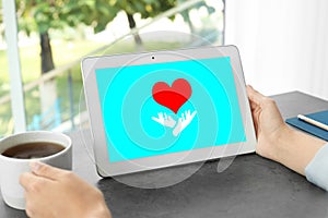 Donations concept. Woman with tablet and cup of coffee at table