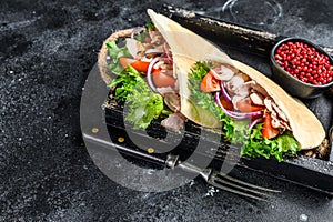Doner kebab with grilled chicken meat and vegetables in pita bread on a wooden tray. Black background. Top view. Copy