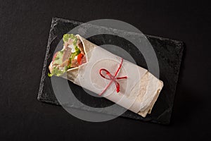 Doner kebab or shawarma sandwich on black slate background.