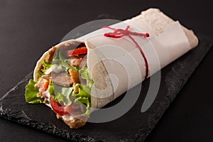 Doner kebab or shawarma sandwich on black slate background.