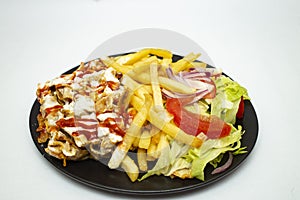 Donner kebab with chips and salad, on a black plate isolated on white background.