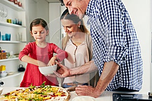 Dont forget the cheese. a cheerful family preparing a pizza together to go into the oven in the kitchen at home.