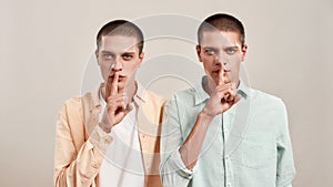 Dont tell anyone. Portrait of two young twin brothers holding finger on lips and making hush gesture while posing