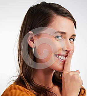 Dont tell a soul. Studio shot of a young woman smiling and signalling to be quiet against a background.