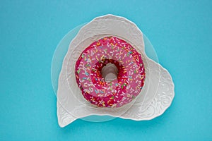 Donut with colorful sprinkles isolated lying on a white plate on blue background. Top view