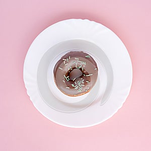 Donut covered with chocolate glaze and sprinkled with green tubes on white plate