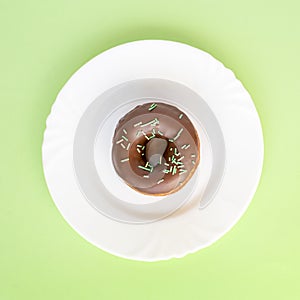 Donut covered with chocolate glaze and sprinkled with green tubes on white plate photo