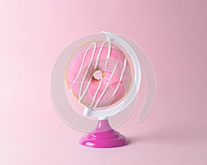 Donut on a globe stand on pastel pink background. Minimal concept