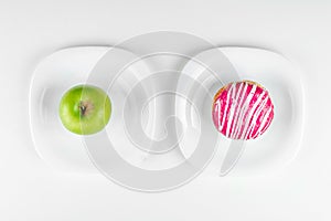 A donut and a green apple lie on the plates top view, the right choice. Concept Resistance to temptation, fast food, healthy food