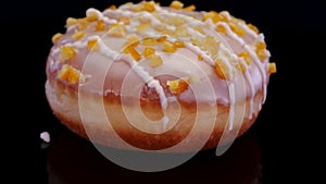 Donut with icing and orange peel sprinkle rotating on a black background.