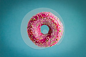 donut with pink berry chocolate icing and sprinkles flying on blue background