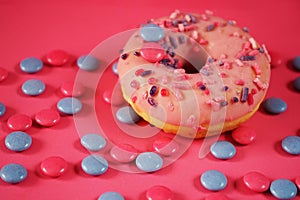 Donut with pink icing and sprinkles next to scattered candies