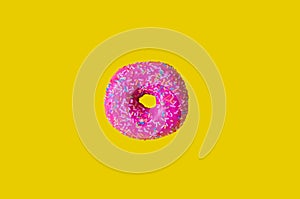 Donut with pink icing on a yellow background top view. Junk food. Sweets, pastries