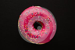 Donut pink with sprinkles isolated on black background, close-up